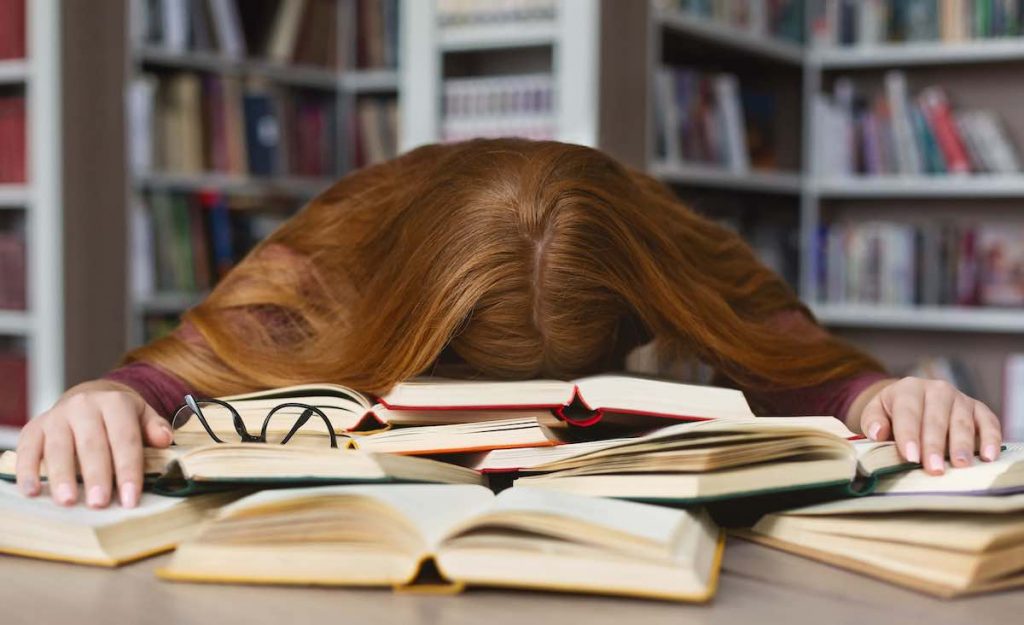 Extremely tired caucasian girl sleeping on books at library